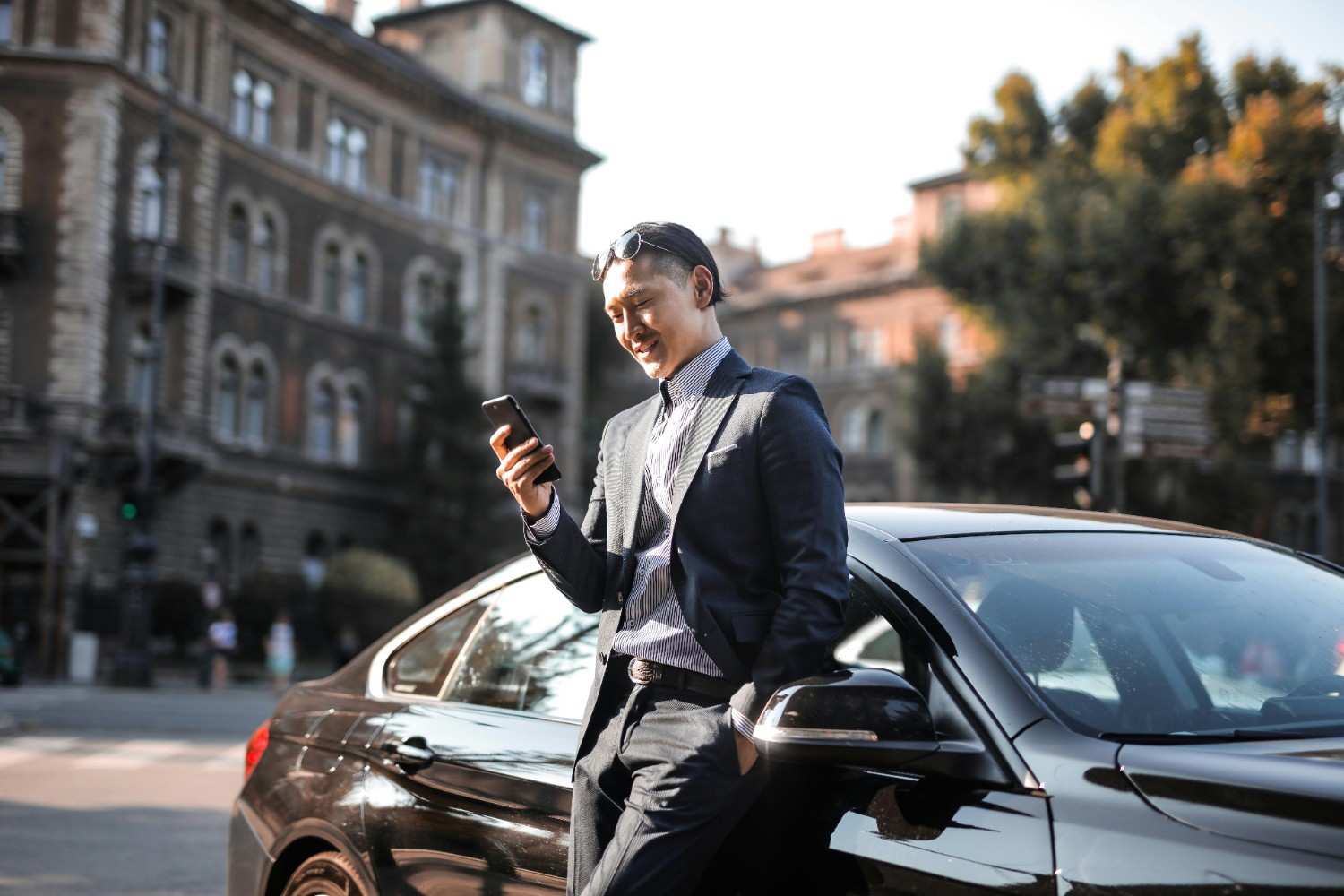 A happy driver smiling while looking at their phone and leaning against a modern car
